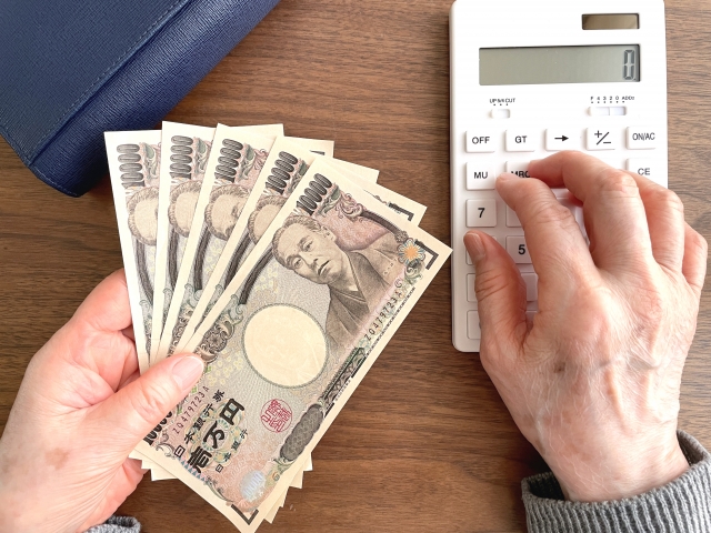 1万円札を持ち、計算機で計算をしている手元