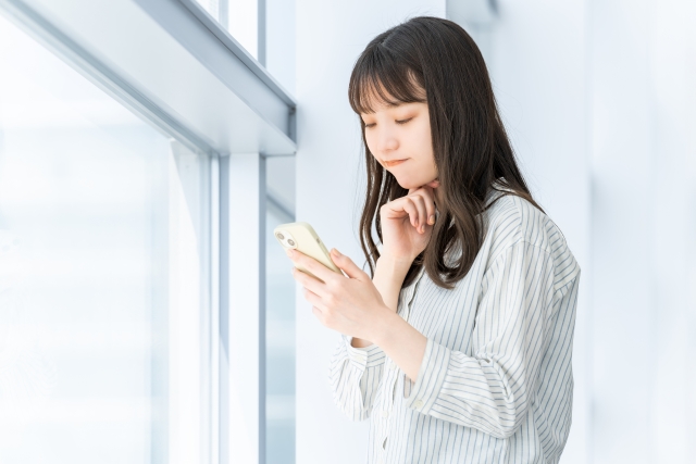 スマホの画面を見て悩んでいる様子の女性