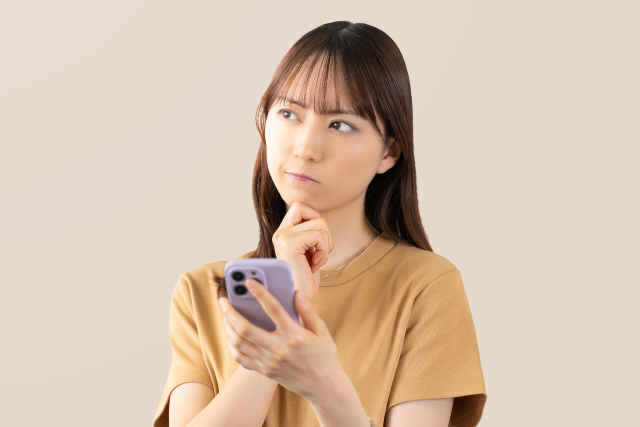 スマホを見ながら悩んでいる表情の女性の画像