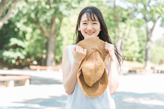 麦わら帽子を両手で持ってカメラ目線で笑顔の女性の画像