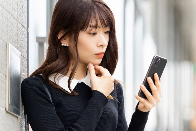 悩んでいる表情でスマホを見る女性の画像